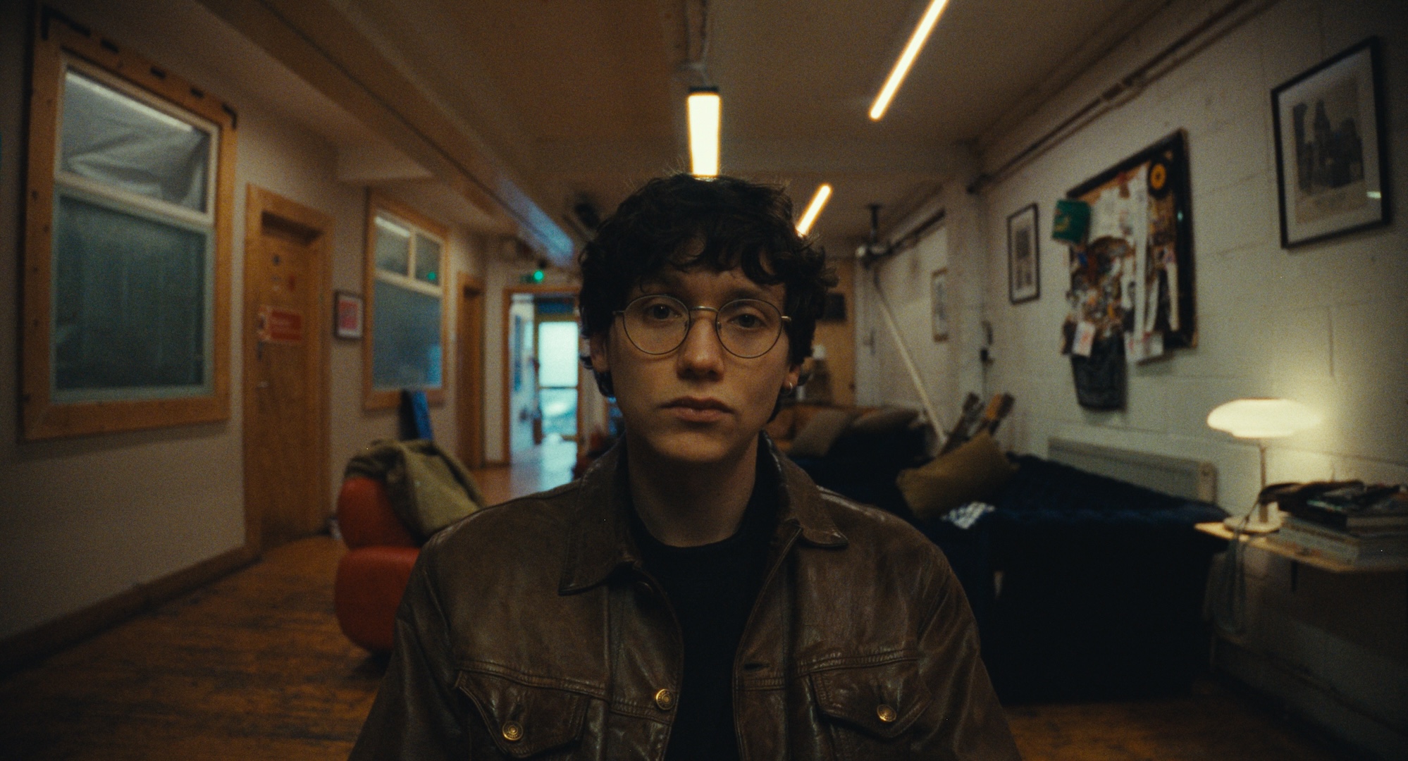 A man wearing glasses in an interior corridor, from All Included