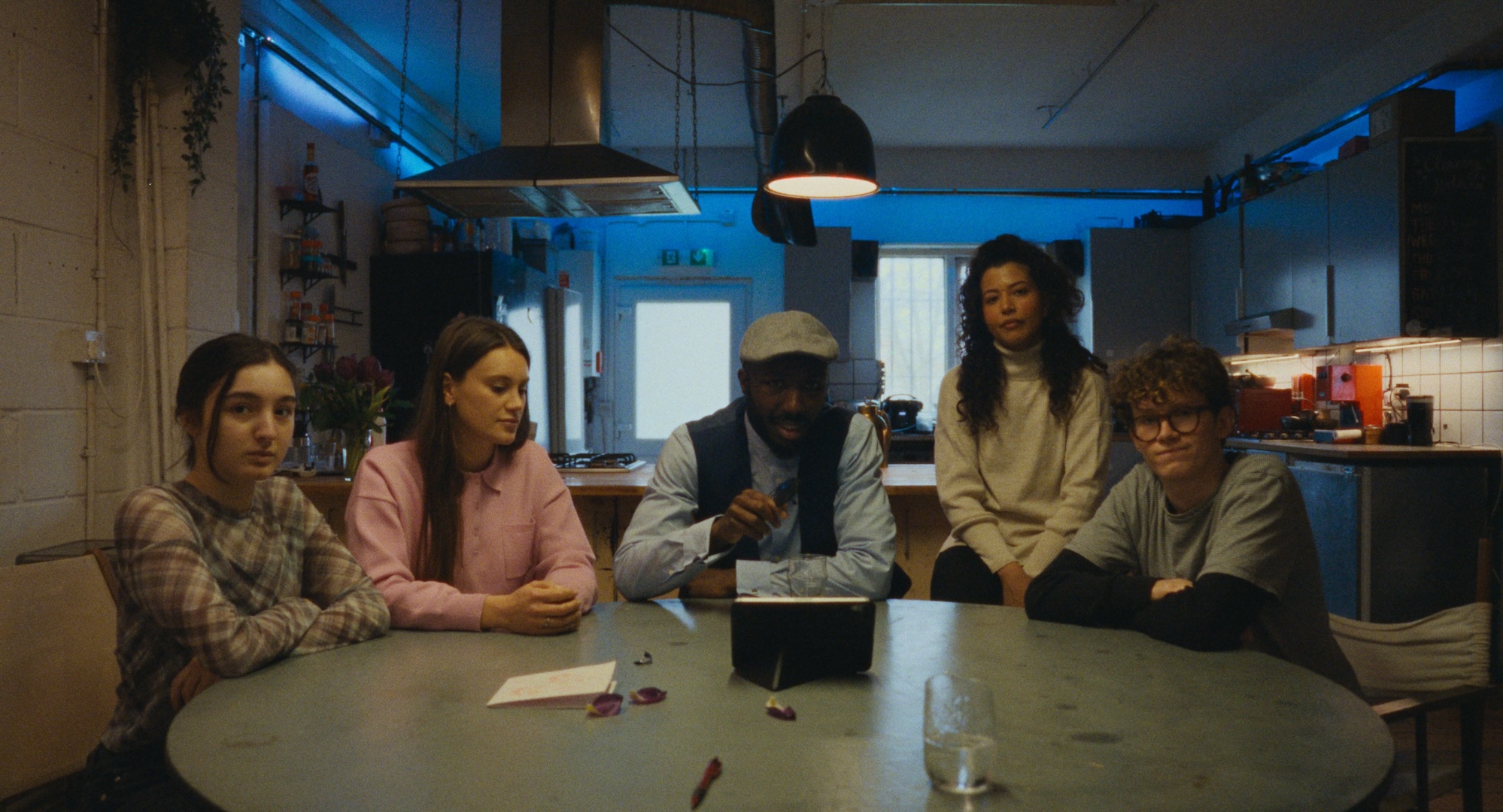 Five people gathered around a kitchen table, from All Included