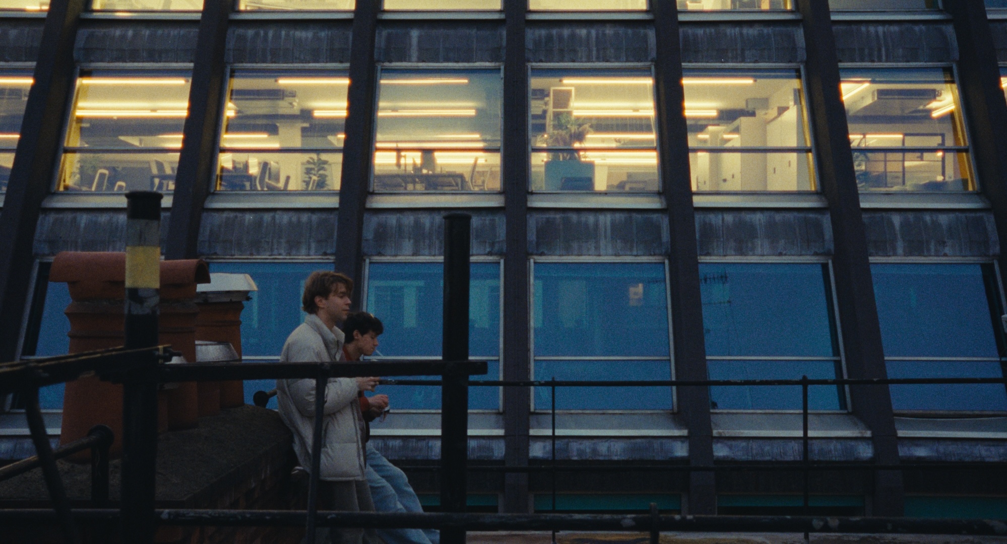 Two men on a rooftop beside an illuminated building, from All Included