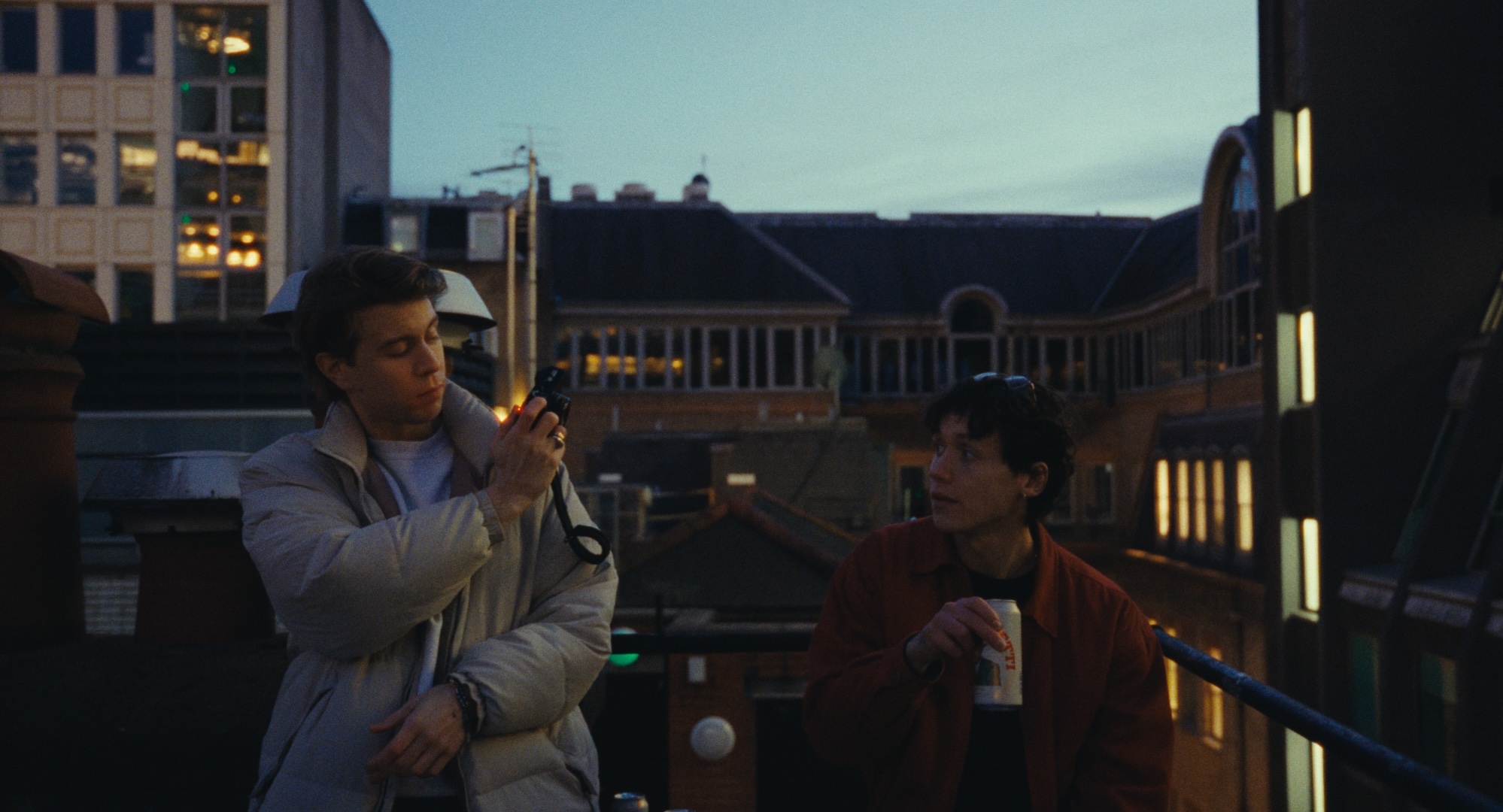 Two men on a London rooftop at dusk, one holding a camera, from All Included